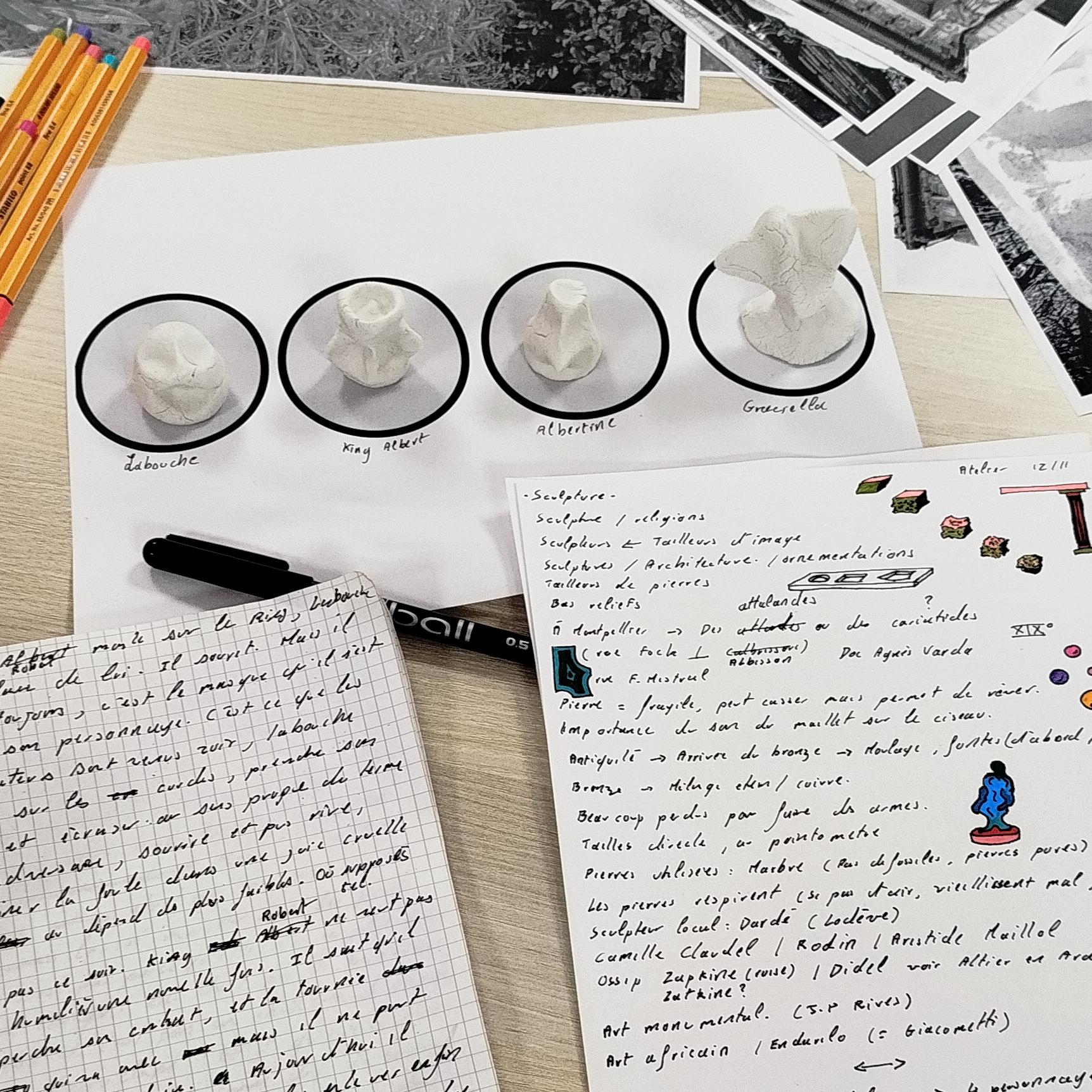 Posés sur une table, des feutres, des photos de sculptures, 4 personnages en pâte à modeler et des notes prises sur des feuilles et sur un carnet